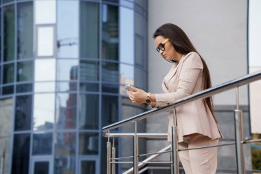 Modern bir ofis binasının önünde Mobil İletişimde Bulunan Profesyonel Kadın.