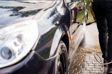 Güneşli bir günde yüksek basınçlı çamaşır makinesiyle araba temizleyen bir insan..