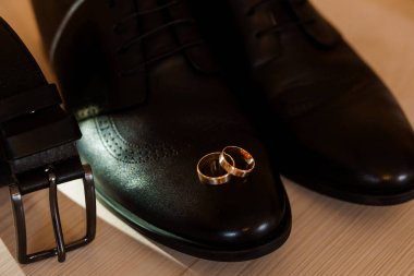 Ayakkabılı, kemerli ve altın yüzüklü zarif düğün detayları.