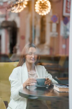 Serene Reflection of a Woman Enjoying Coffee in a Cozy Cafe Setting. clipart