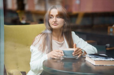 Samimi bir kafede kahve içen düşünceli bir kadının yansıması..