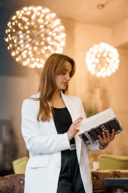 Zarif Beyaz Ceketli Kadın Şık Işıklar Altında Kitap Okuyor.