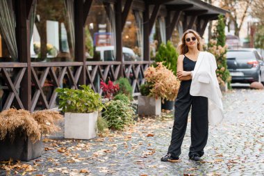 Cobblestone Caddesi 'nde dikilen Şık Giysili Kadın Sonbahar Yeşilleriyle çevrili.