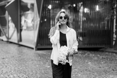 Şık Kadın Şehir Ayarlarında Telefonda Konuşurken Çiçekleri Tutuyor.