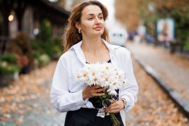 Beyaz tişörtlü, Papatyaları Yapraklı Yol 'da Tutan Serene Genç Kadın.