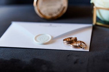 Zarifçe düzenlenmiş evlilik yüzükleri ve kadife arka planda mühürlü davetiyeler..