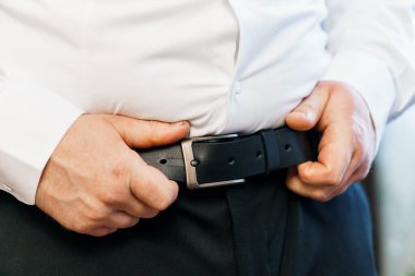 Beyaz elbiseli bir adam kemerini ayarlıyor..