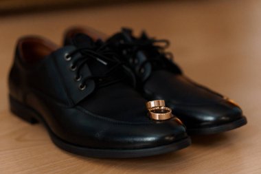 Ahşap zeminde alyansları olan zarif siyah elbiseli ayakkabılar..