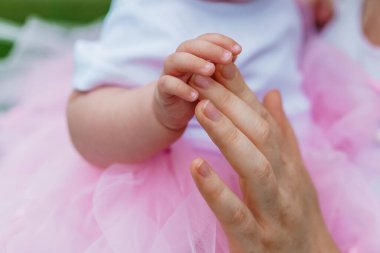 Şefkatli Anlar: Bir Bebeğin Eli Yetişkin Parmağını Yumuşak Pembe Tutu İçinde Tutuyor.