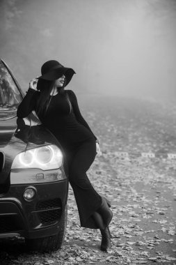 Siyah Giysili Zarif Kadın Puslu Sonbahar Ortamı 'nda Lüks bir SUV Pozisyonu.