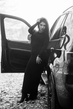 Siyah elbiseli zarif kadın gizemli bir atmosferde arabanın yanında poz veriyor..