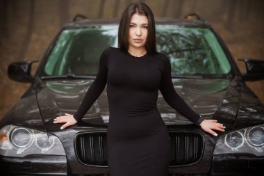 Woman in Black Dress Posing Confidently in Front of a Black SUV in an Enigmatic Forest Setting. clipart