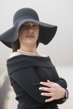 Siyah Şapkalı Zarif Kadın ve Omuzsuz Süveter Puslu Bir Arkaplan Karşısında.