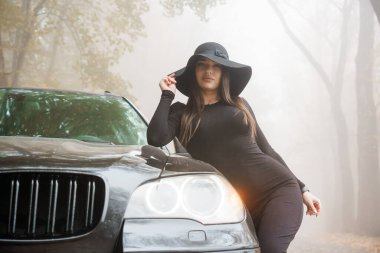 Esrarengiz Zarafet: Sisli Ormanın Ortasında Siyah Bir Araba Tarzı Tarz Eden Bir Kadın.