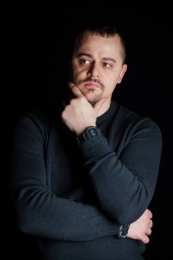 Siyah Süveterli Düşünceli Adam Karanlık Arkaplana Karşı Düşünceli İfadesiyle Pozisyon Veriyor.