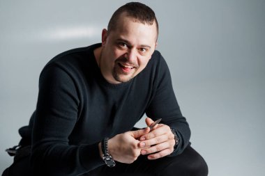 Bıçaklı gülümseyen adam, rahat duruşuyla yerde oturuyor..