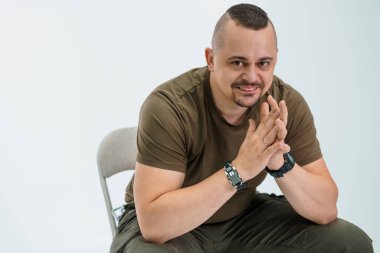 Elleri Birarada Sandalyede Oturan Gündelik Giysili Kendine Güvenen Adam.