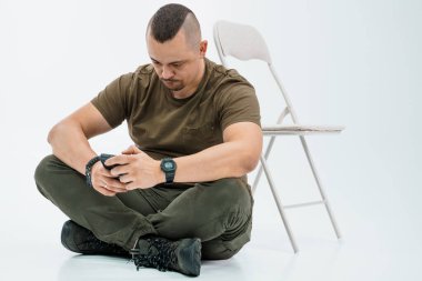 Bir sandalyenin yanında otururken akıllı telefon kullanan odaklanmış bir adam..