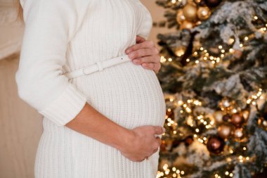 Noel Ağacı Arkaplanlı Beyaz Elbiseli Hamile Kadın.