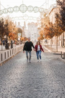 Sonbaharda kaldırım taşı caddesinde el ele koşan neşeli çift.