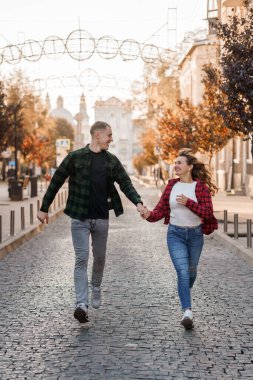 Sonbaharda kaldırım taşı caddesinde el ele koşan neşeli genç çift..
