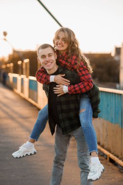 Genç çift gün batımında bir köprüde neşeli bir anı paylaşıyor, sevgi ve mutluluk sergiliyorlar..