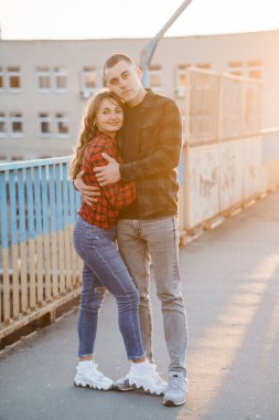 Güneşli bir köprüde kucaklaşan genç bir çift.