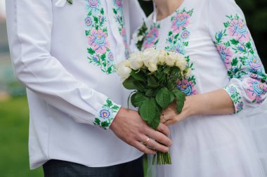 Geleneksel Nakışlı Giysiler ve Beyaz Gül Buketi içeren Zarif Açık Hava Düğün Töreni.