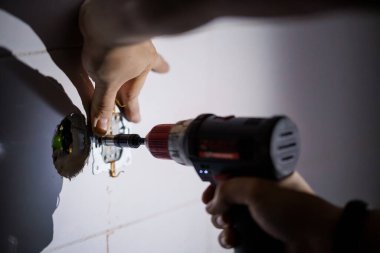 Hand holding a power drill while installing a wall socket in a home renovation project. clipart