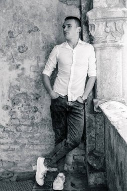 Zarif bir genç adam yıpranmış bir duvara karşı zarif bir şekilde poz veriyor..