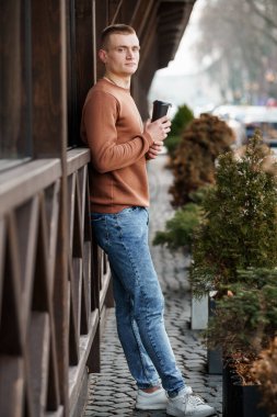 Kırsal bir ahşap binanın yanında, Kahveyle Rahatlayan Genç Adam.