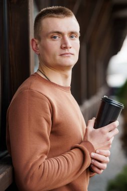 Kahve fincanlı genç adam Düşünceli bir şekilde bir pencerenin yanında poz veriyor.