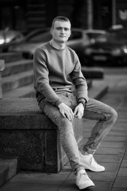 Şehir ortamında beton basamaklarda oturan günlük kıyafetli genç adam..