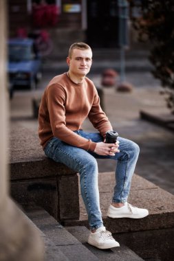 Genç adam kahve fincanı ile merdivenlerde oturuyor..