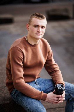 Genç adam şehir ortamında elinde kahve fincanıyla öylesine oturuyor..