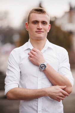 Beyaz Gömlekli Güvenilir Genç Adam Şehir Ayarlarında Saati Gösteriyor.