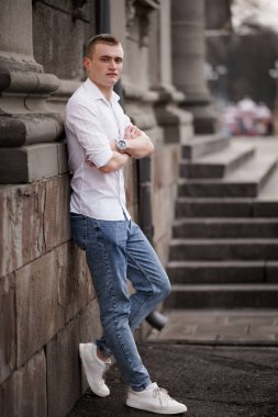 Günlük kıyafetli genç adam tarihi bir duvara yaslanıyor..