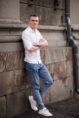 Gündelik kıyafetli genç adam, dokulu taş bir duvara yaslanıyor..