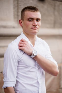Beyaz gömlekli, kendine güvenen genç adam dışarıda poz veriyor..