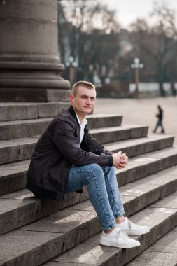 Genç adam şehir merkezinde taş basamaklarda öylesine oturuyor..