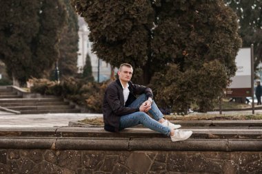 Düşünceli Genç Adam Parktaki Taş Duvarda Oturuyor.