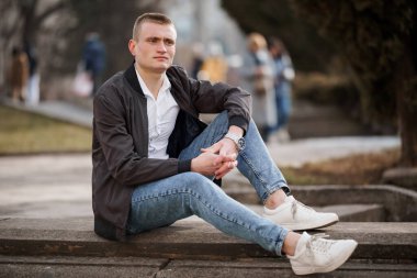 Günlük kıyafetli genç adam dışarıda, parkta oturuyor..