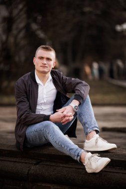 Açık havada oturan genç bir adamın sıradan portresi..