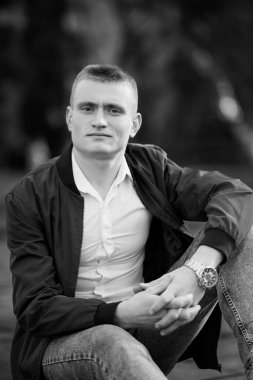 Gündelik kıyafetli genç adam dışarıda oturmuş, derin bir ifadeyle..