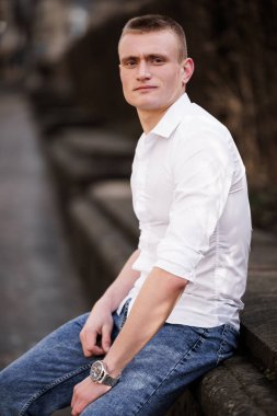 Günlük kıyafetli genç adam kendine güvenen bir görünümü olan açık havada poz veriyor..