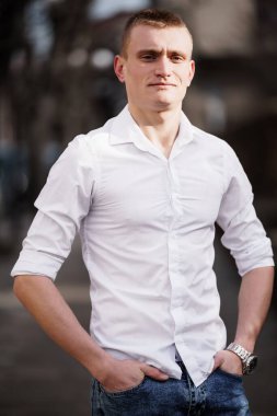 Beyaz gömlekli, kendine güvenen genç adam dışarıda poz veriyor..