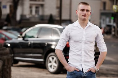 Şehir merkezinde lüks bir cipin yanında poz veren kendinden emin genç adam..