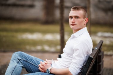 Parktaki bir bankta kendinden emin oturan genç adam..