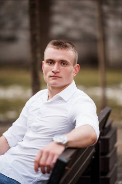 Günlük kıyafetlerle park bankında oturan genç bir adamın portresi..