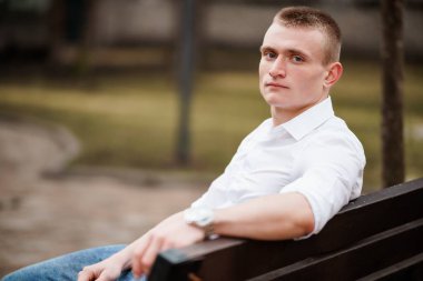 Günlük kıyafetli dalgın genç adam Park Bench 'inde oturuyor..